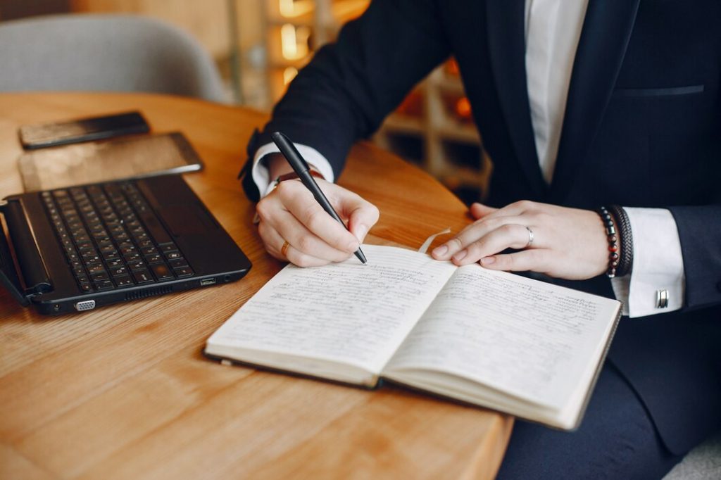 Person using a phone beside a laptop and notebook