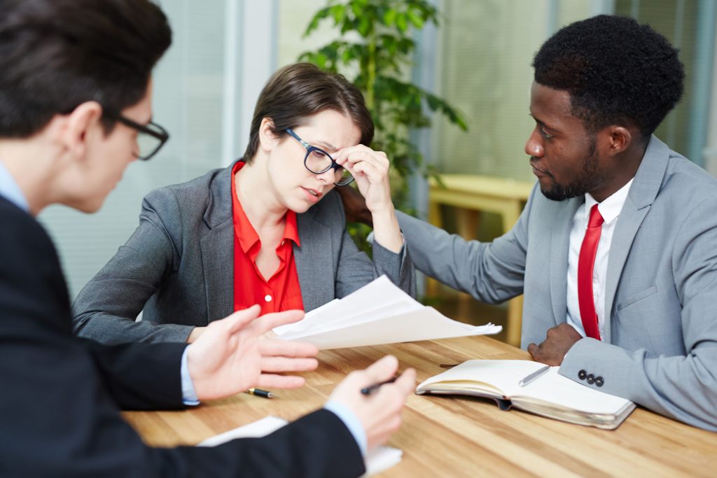Three people in a tense meeting across a desk