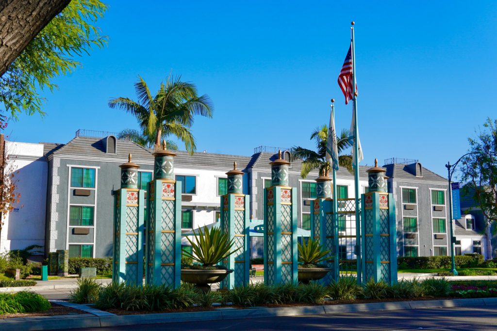 A multistory hotel building for a business lawyer in Alhambra viewed behind a decorative teal fence and potted agave plants, with the American flag flying on a pole.