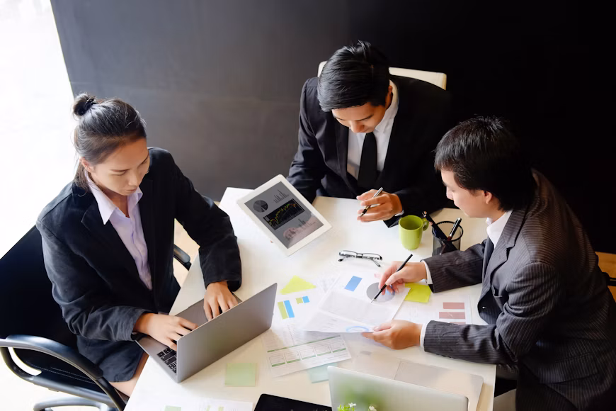 Three business lawyers in Lakewood collaborate around a desk with laptops, charts, and a tablet.