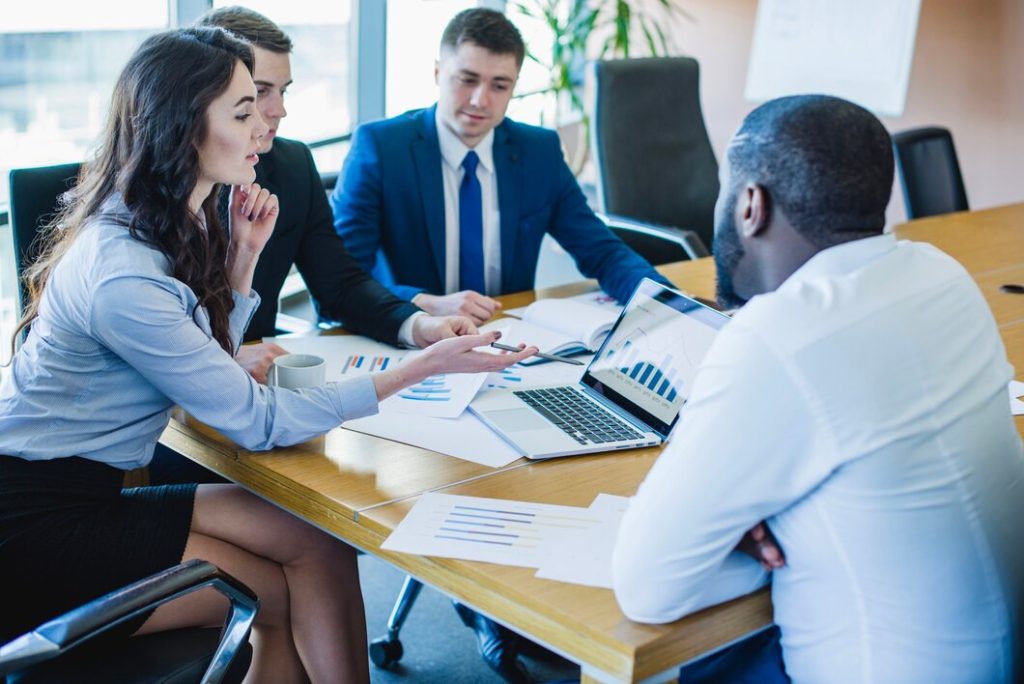 Four people sitting around a conference table with a business lawyer in Los Feliz, looking at charts on a laptop and printed documents.