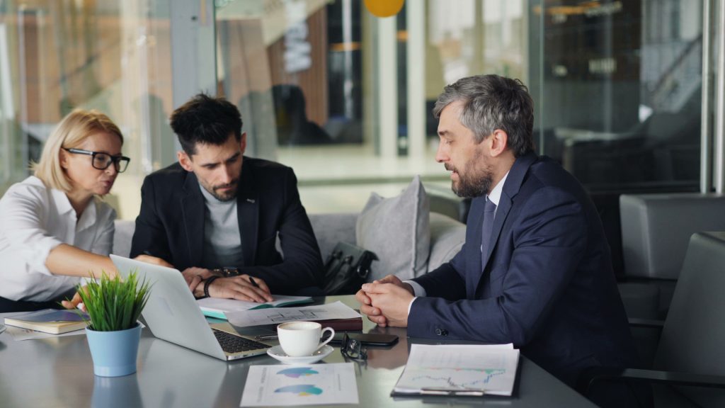 A Manhattan Beach business lawyer sits with two colleagues around an office table to review documents and a laptop.