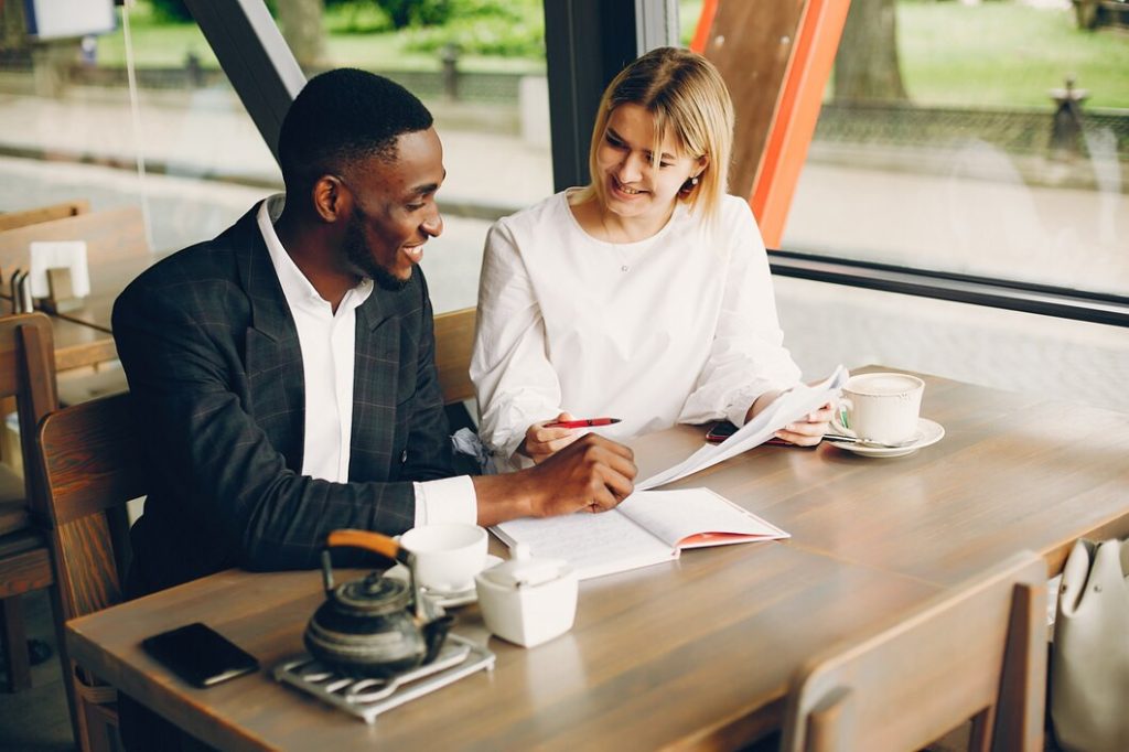 A business lawyer in North Hollywood and a woman in a white blouse sitting at a cafe table, reviewing documents together.