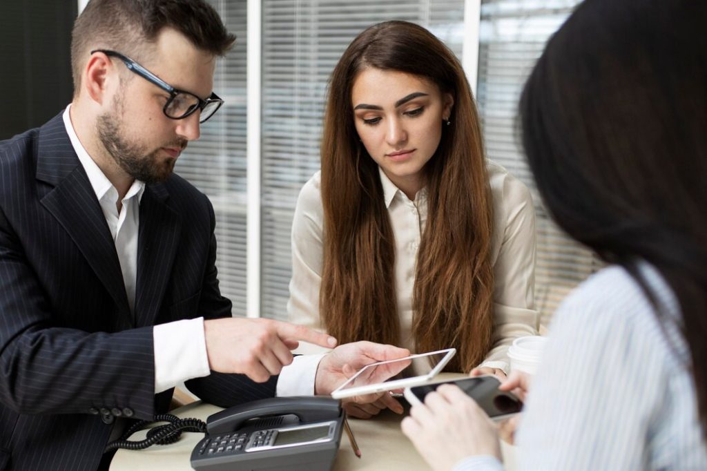 Three business professionals, including a business lawyer in Northridge, looking at a tablet and a smartphone in an office.