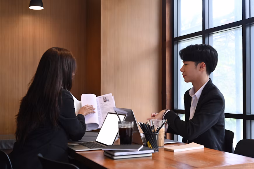 A business lawyer in Palms and a woman in business attire sitting at a table with laptops and documents, having a meeting.