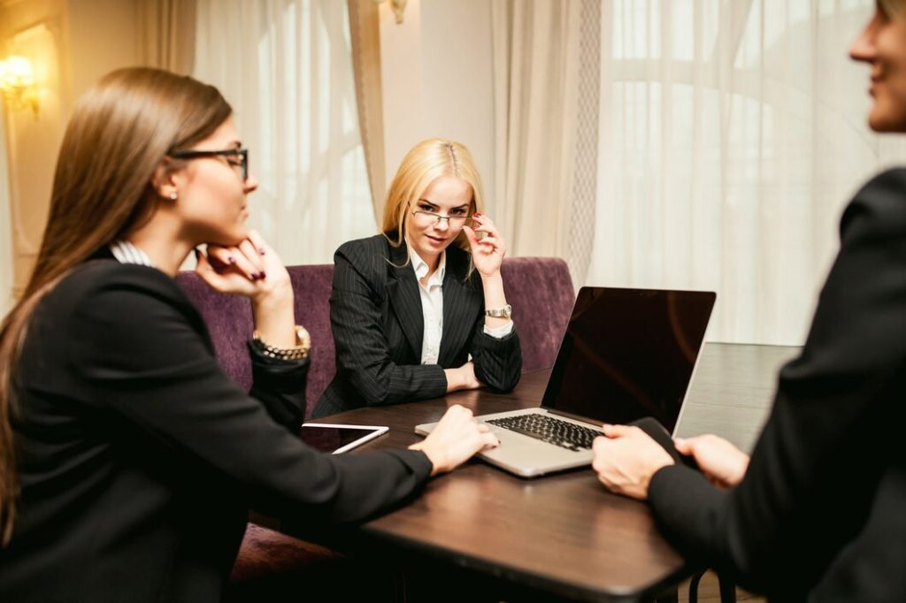 Three businesswomen in suits sit around a conference table with a laptop, meeting with a business lawyer in Pomona.