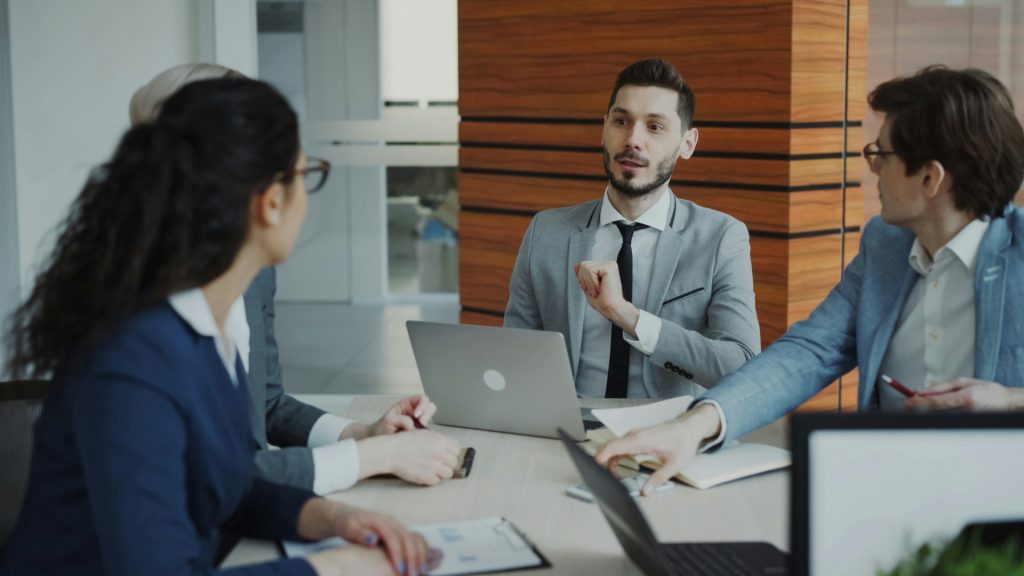 A business lawyer in Porter Ranch gestures while speaking to three professionals seated around a conference table during a meeting.