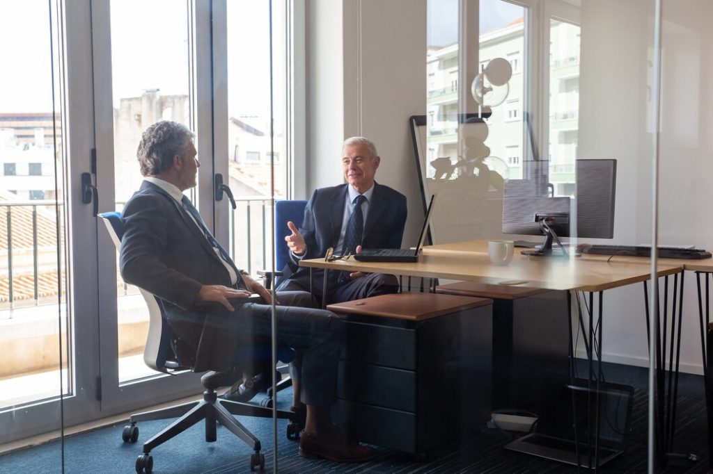 Two men in business suits, including a business lawyer in San Dimas, talking across an office desk.