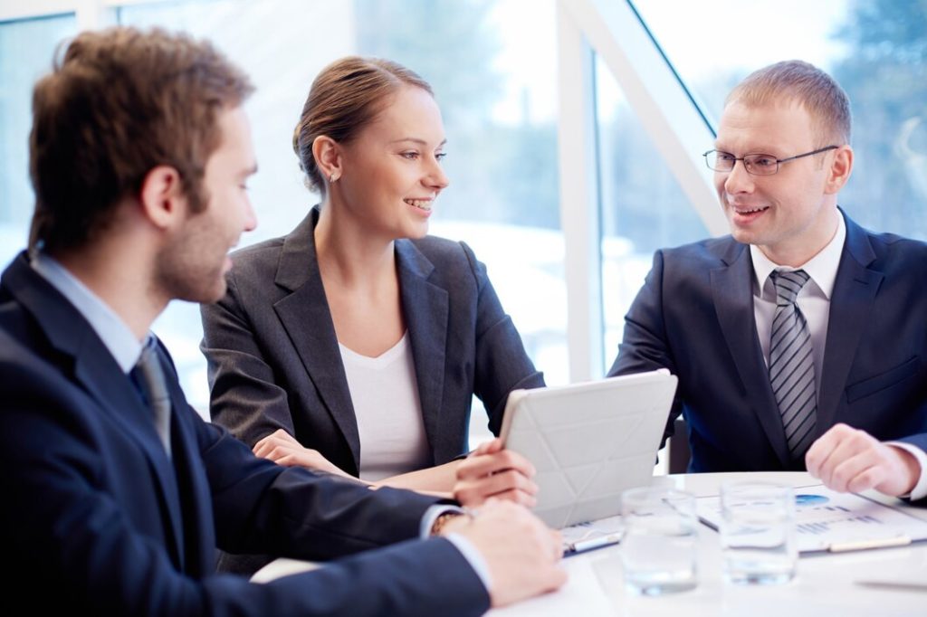 Three business lawyers in Santa Monica sit at a round table, discussing information on a tablet.