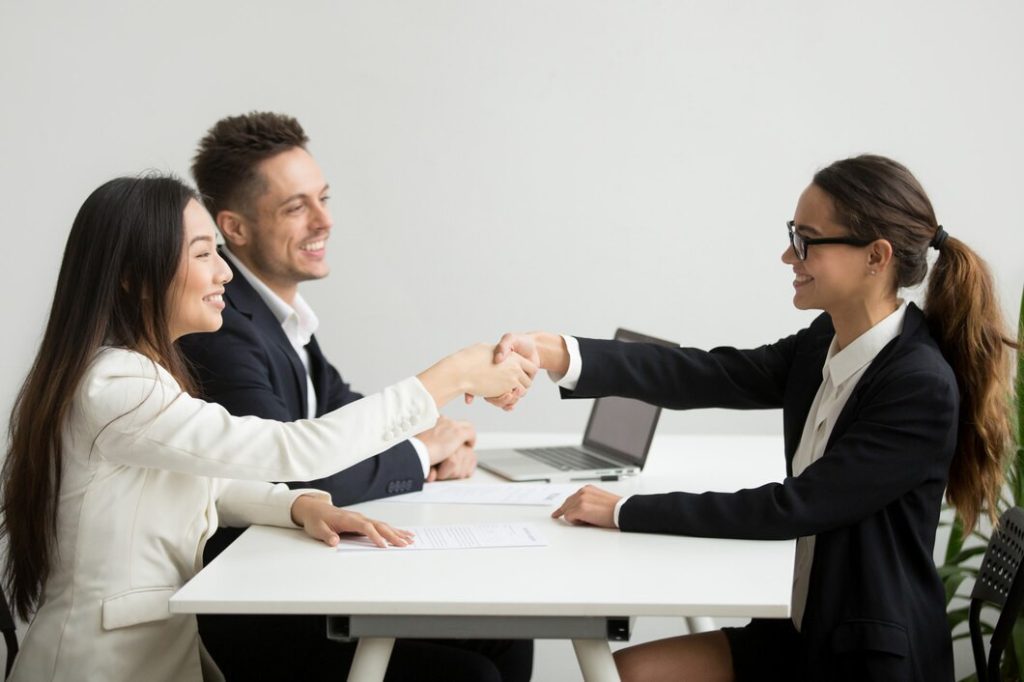 Two women shaking hands across a desk while a business lawyer in Silver Lake looks on and smiles.