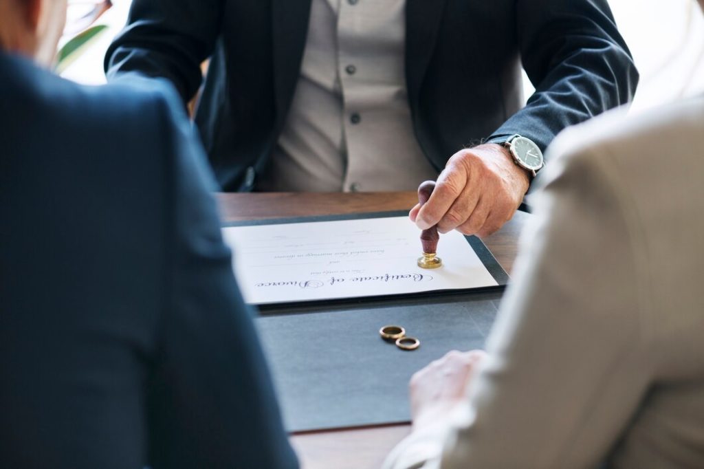 A hand stamps a Certificate of Divorce on a desk beside two wedding rings, a scene often handled by a Business Lawyer in Tarzana.