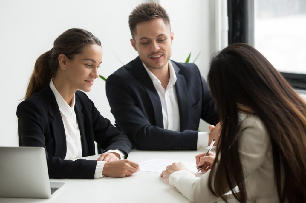 A woman signs a document at a table while two business professionals from a Van Nuys lawyer office look on.