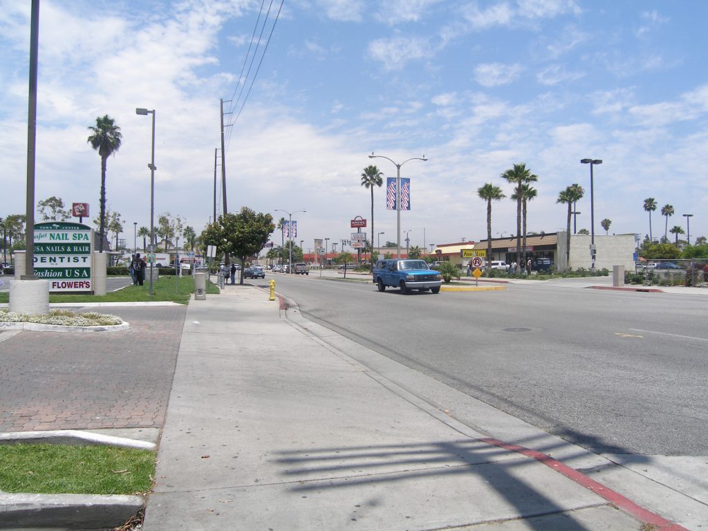 A blue pickup truck drives past a shopping center with a tall sign listing local businesses, including a business lawyer in Carson.