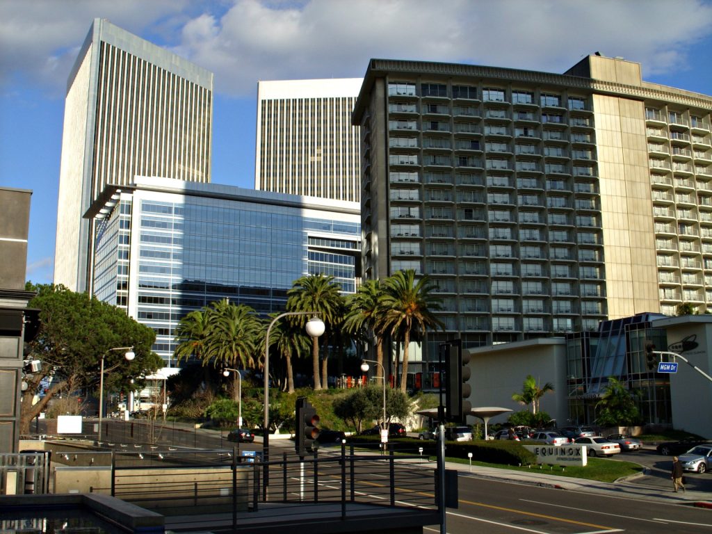 A view of city office buildings and a hotel near a business lawyer in Century City, with palm trees and a road intersection in the foreground.