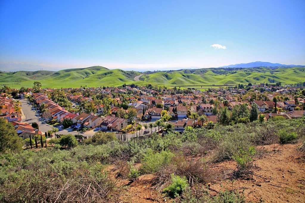 A suburban neighborhood, home to a business lawyer in Diamond Bar, nestled in a valley surrounded by rolling green hills under a clear blue sky.