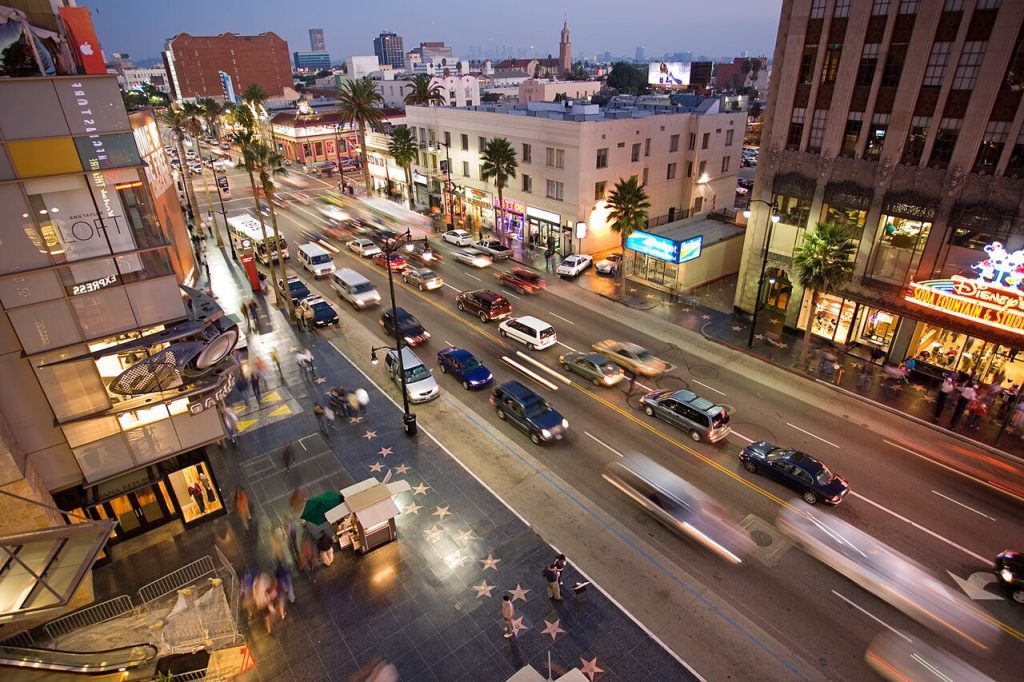High-angle view of Hollywood Boulevard at dusk, with moving traffic, pedestrians on the Walk of Fame, and illuminated storefronts near a business lawyer in Hollywood.