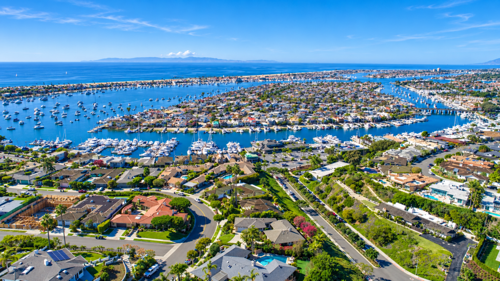 Aerial view of residential homes near a harbor with boats, the ocean, and mountains, in a coastal area served by a Business Lawyer in Orange.
