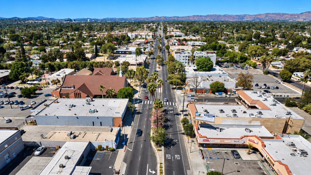 Aerial view of a palm-lined street in Reseda, featuring low-rise buildings and parking lots surrounded by distant hills.