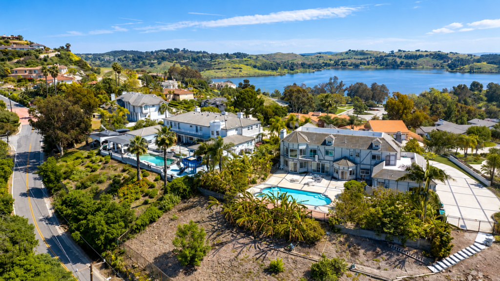 Aerial view of suburban houses, home to a business lawyer in San Dimas, with swimming pools overlooking a large lake and hilly landscape.
