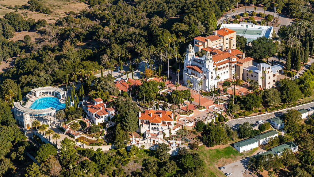 Aerial view of Hearst Castle and its grounds, including the Neptune Pool, surrounded by wooded hills near the San Gabriel Valley.
