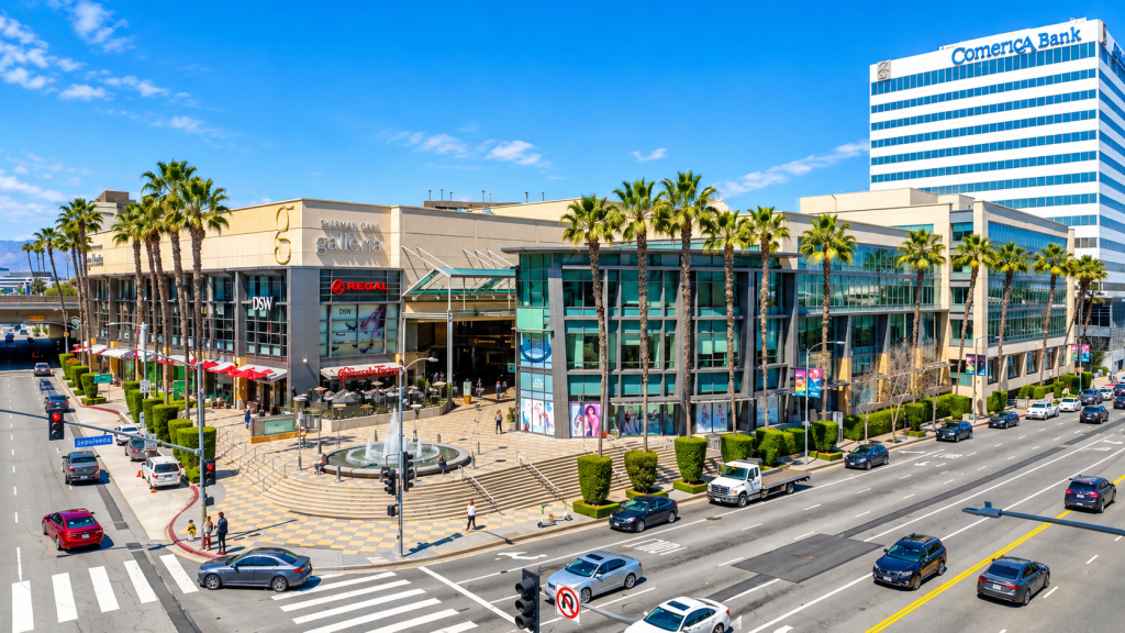 The Sherman Oaks Galleria shopping center, featuring retail storefronts, a central fountain, and palm trees, with a Comerica Bank tower in the background, near a business lawyer in Sherman Oaks.