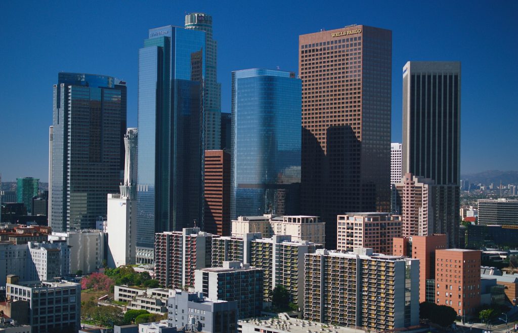 The downtown Los Angeles skyline with various glass and concrete skyscrapers under a clear blue sky.