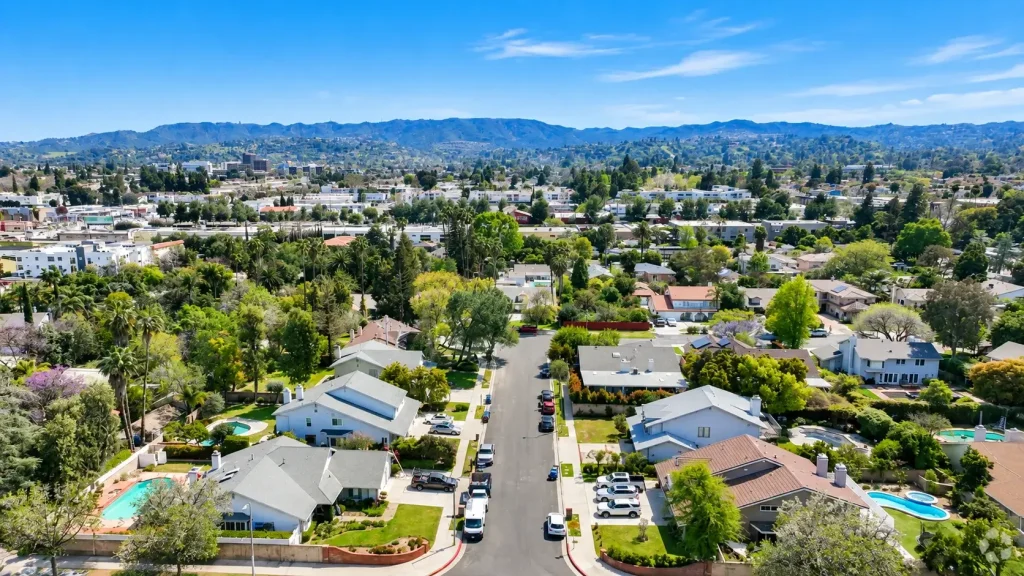 Aerial view of a residential neighborhood near a business lawyer in Tarzana, with houses, palm trees, and hills in the background under a clear blue sky.