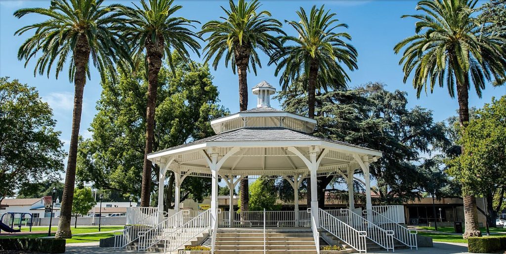 A white gazebo centered in a park surrounded by tall palm trees in Temple City.