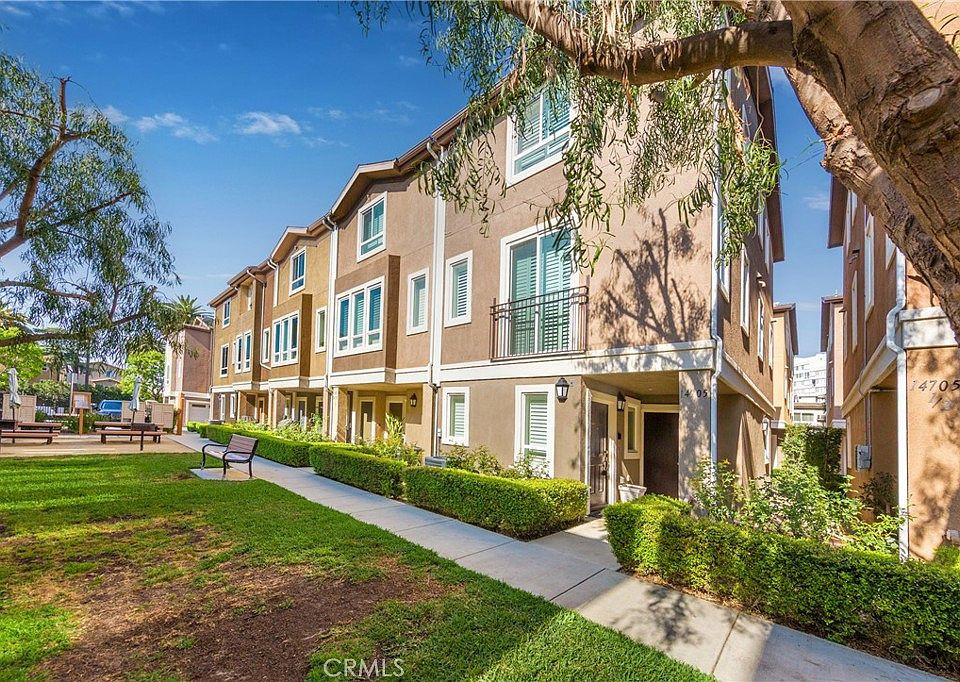 A row of tan, multi-story townhomes with white trim located near a Business Lawyer in Van Nuys, featuring a landscaped lawn, a concrete walkway, and a small patio area.