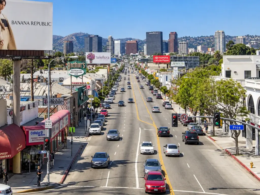 High-angle view of a city street in Westwood, lined with shops and billboards, leading toward a skyline of distant buildings where a business lawyer might work.