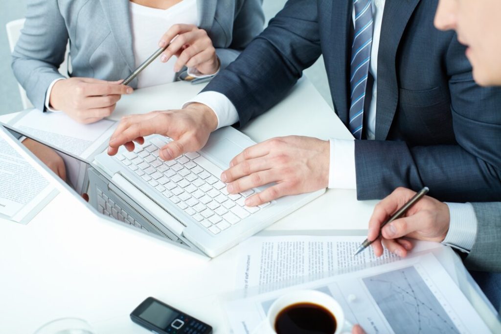 Three business professionals, including a business lawyer in Brentwood, collaborating at a table with a laptop, documents, and a coffee cup.