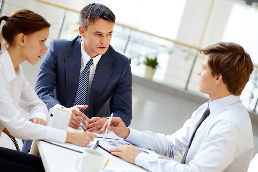 Three colleagues, including a business lawyer in Chatsworth, discussing charts around a table in an office.