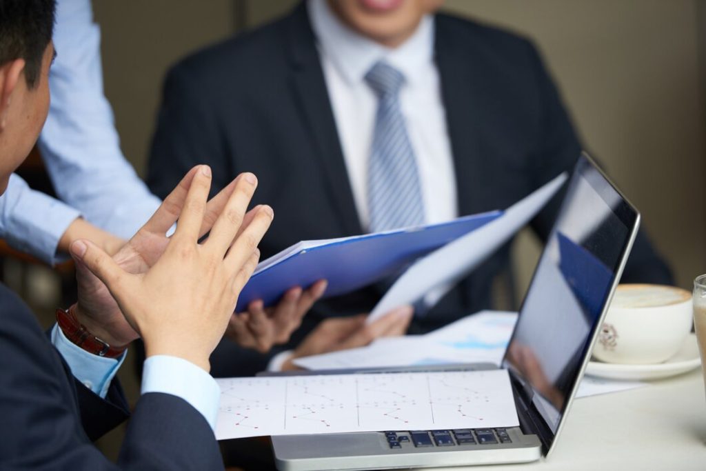 Two business lawyers in Alhambra discuss documents and a laptop displaying data charts during a meeting.
