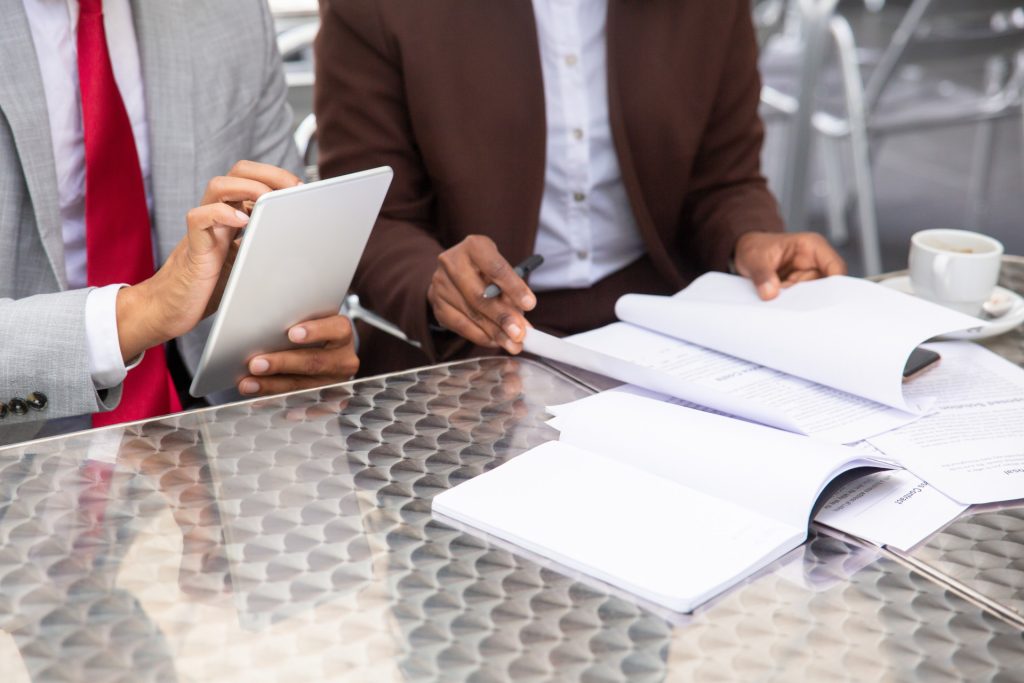 Two business people in suits seated at a table for business litigation in Irvine, one using a tablet and the other reviewing a document.
