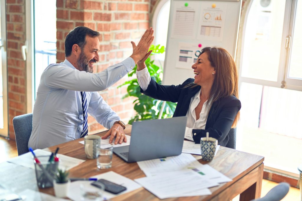 A business litigation lawyer in LA and a woman in professional attire high-five each other across a desk in an office.