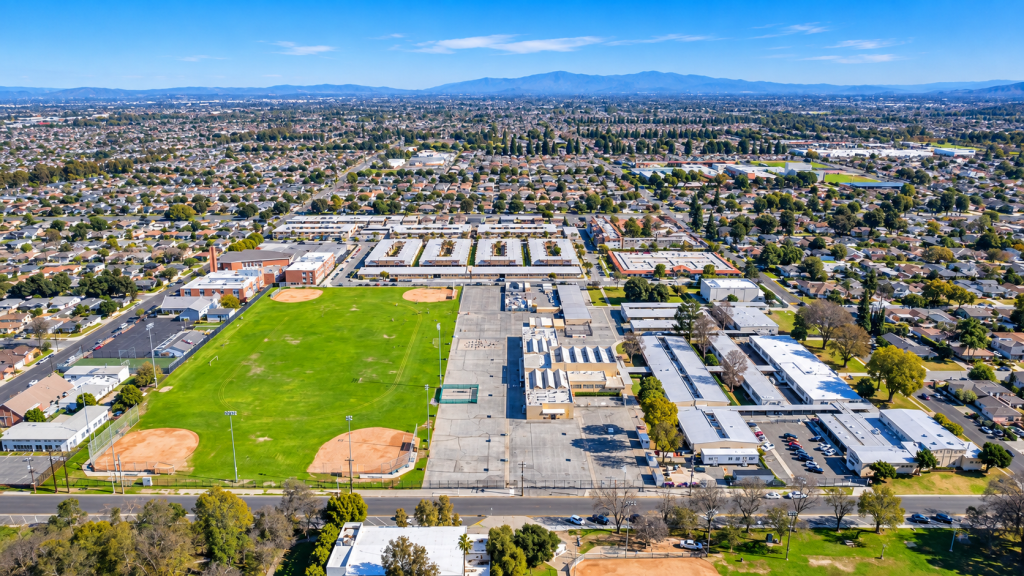Aerial view of a school campus near the office of a business lawyer in Lakewood, featuring athletic fields, a paved courtyard, and surrounding suburban housing under a clear blue sky.