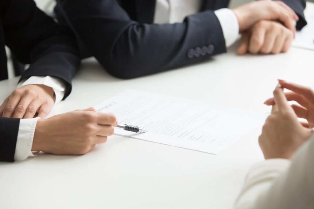 Business professionals sitting at a table with a contract, as a business lawyer in Glendale points to the document with a pen.