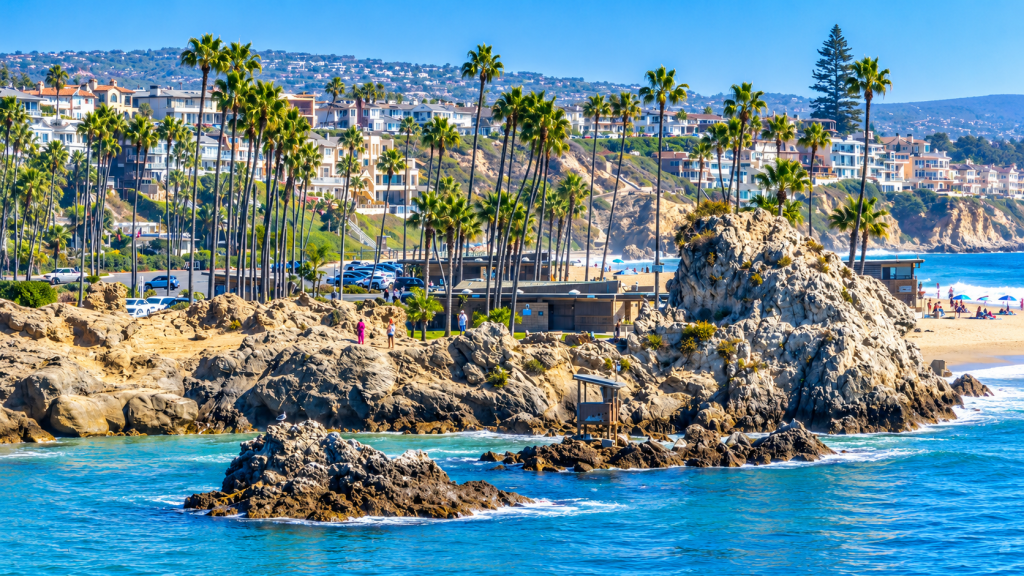 A rocky coastline with palm trees, a beach, and hillside houses in Laguna Beach, near the office of a business lawyer in Newport Beach.