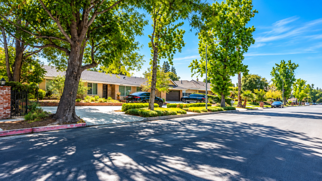 A quiet residential street with single-story homes, mature trees, and parked cars under a clear blue sky, near the office of a business lawyer in Northridge.