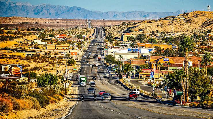A multi-lane highway near a business lawyer in Palms runs through a desert town, featuring surrounding hills and a restaurant sign with a burger and coffee.