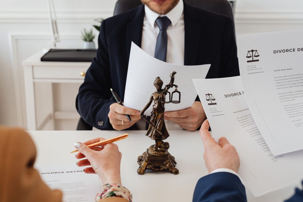A business lawyer in Covina sits at a desk with a bronze Lady Justice statue between two people reviewing divorce documents.