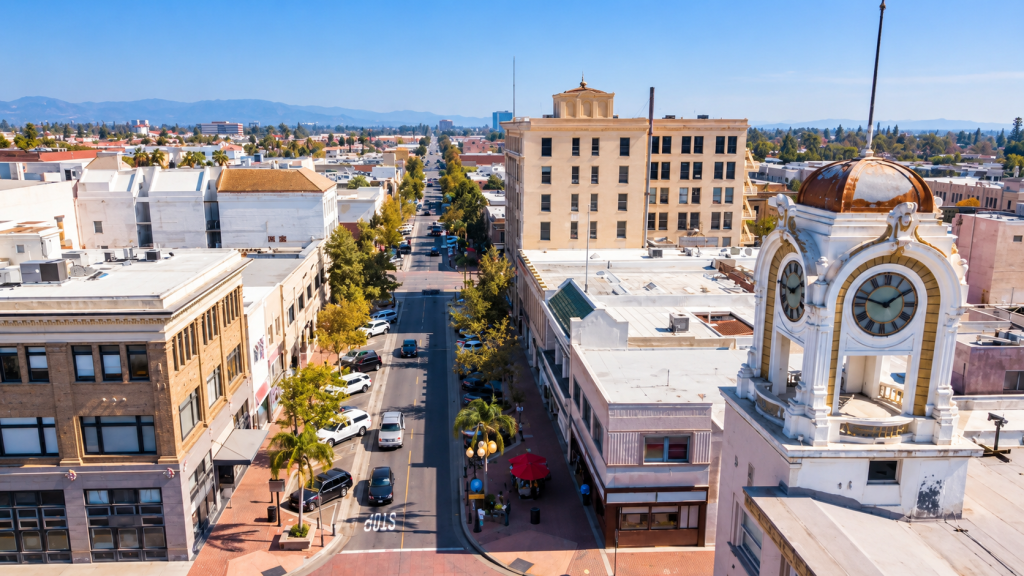 Aerial view of a Santa Ana city street featuring a prominent clock tower in the foreground and mountains in the distance.