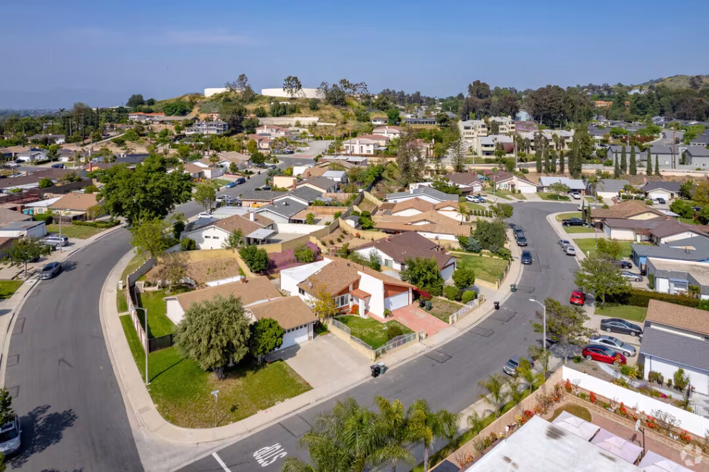 Aerial view of a suburban neighborhood in West Covina with single-family houses, winding roads, and a hillside in the background.