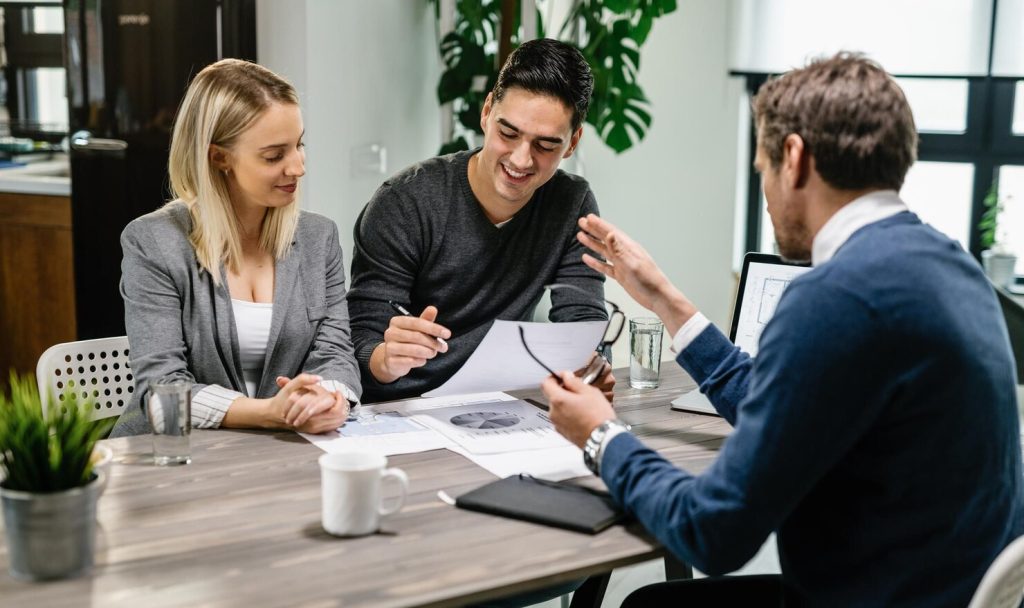 A business lawyer in Costa Mesa gestures while explaining a document to a man and woman during an office meeting.