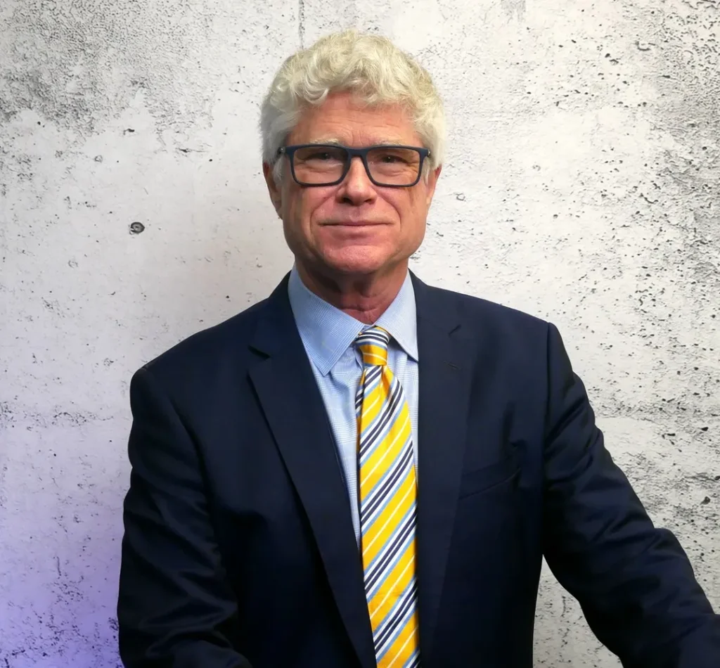 A Lurie & Associates business litigation lawyer with curly grey hair, wearing a navy blue suit, light blue shirt, and a yellow, white, and blue striped tie.